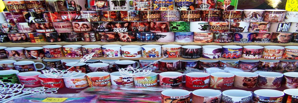 Stoiska z kolorowymi kubkami przedstawiającymi postacie z filmów, gier i seriali telewizyjnych, z różnorodnymi wzorami i tematyką.